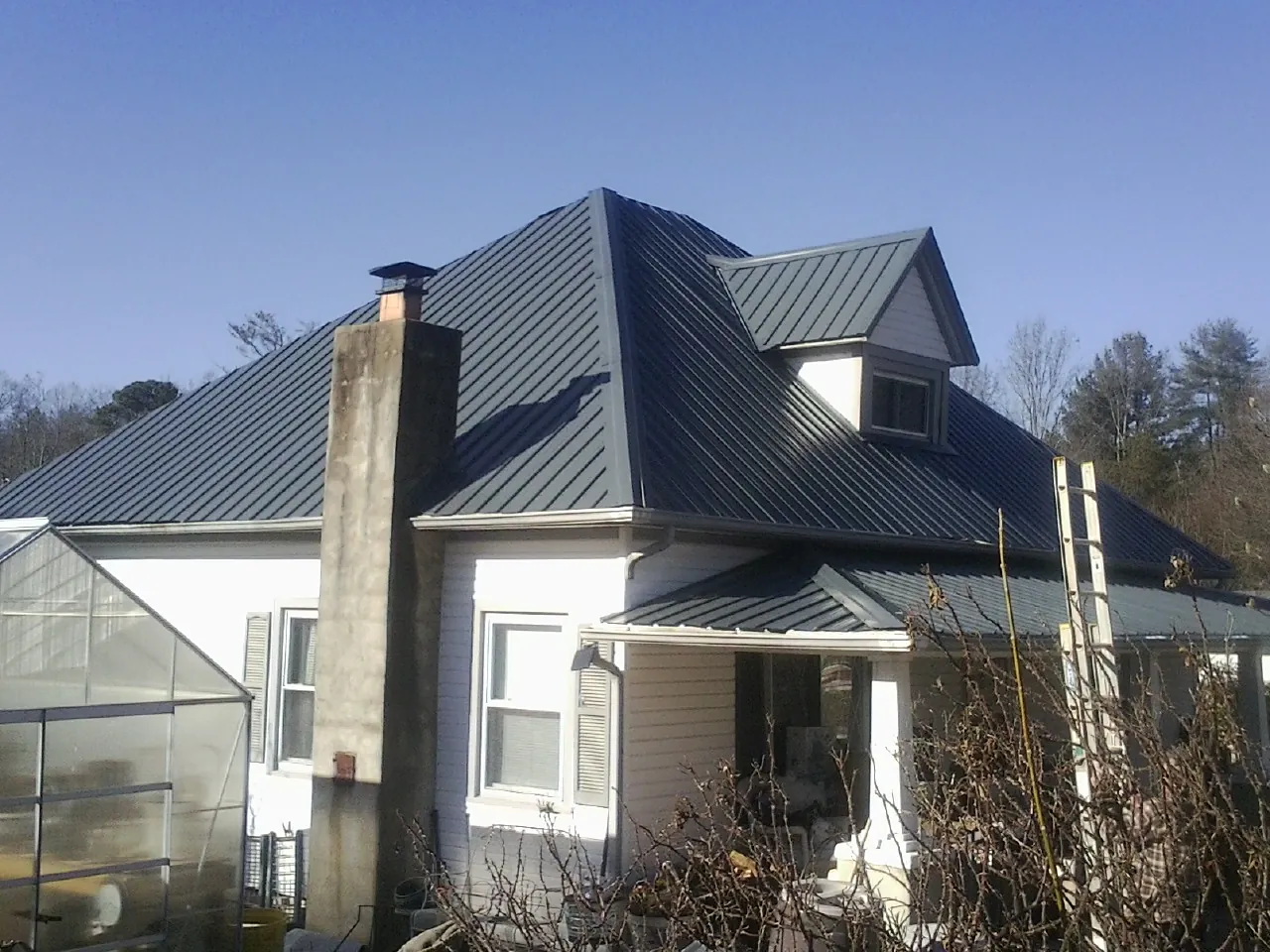 Dark blue standing seam metal roof on a white farmhouse with dormer — Slate & Tile Roof Repair by Roofing Brothers in Royal Oak