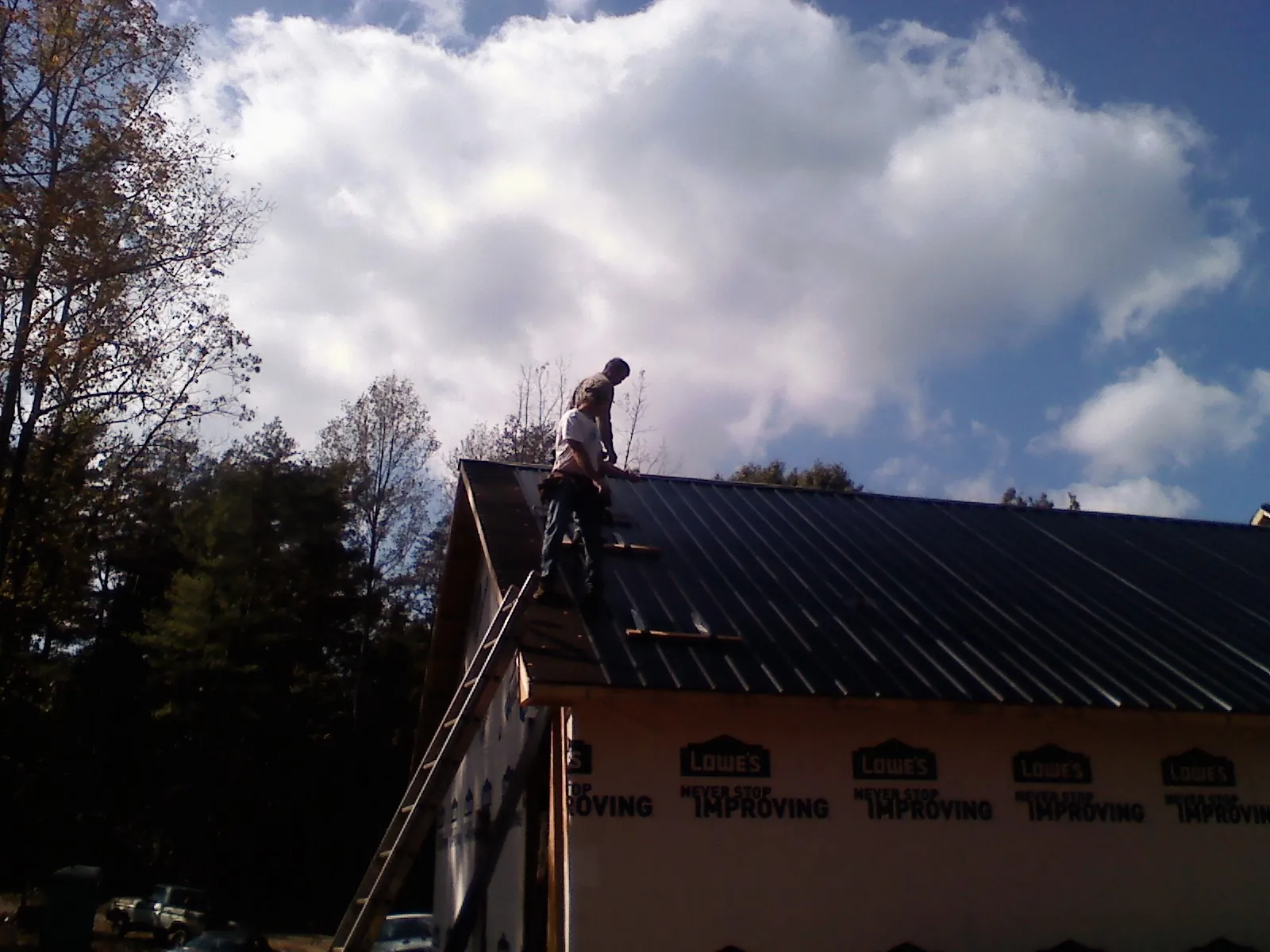 Roofer fastening dark metal panels high against a cloudy sky, from a Roof Inspection job in Royal Oak