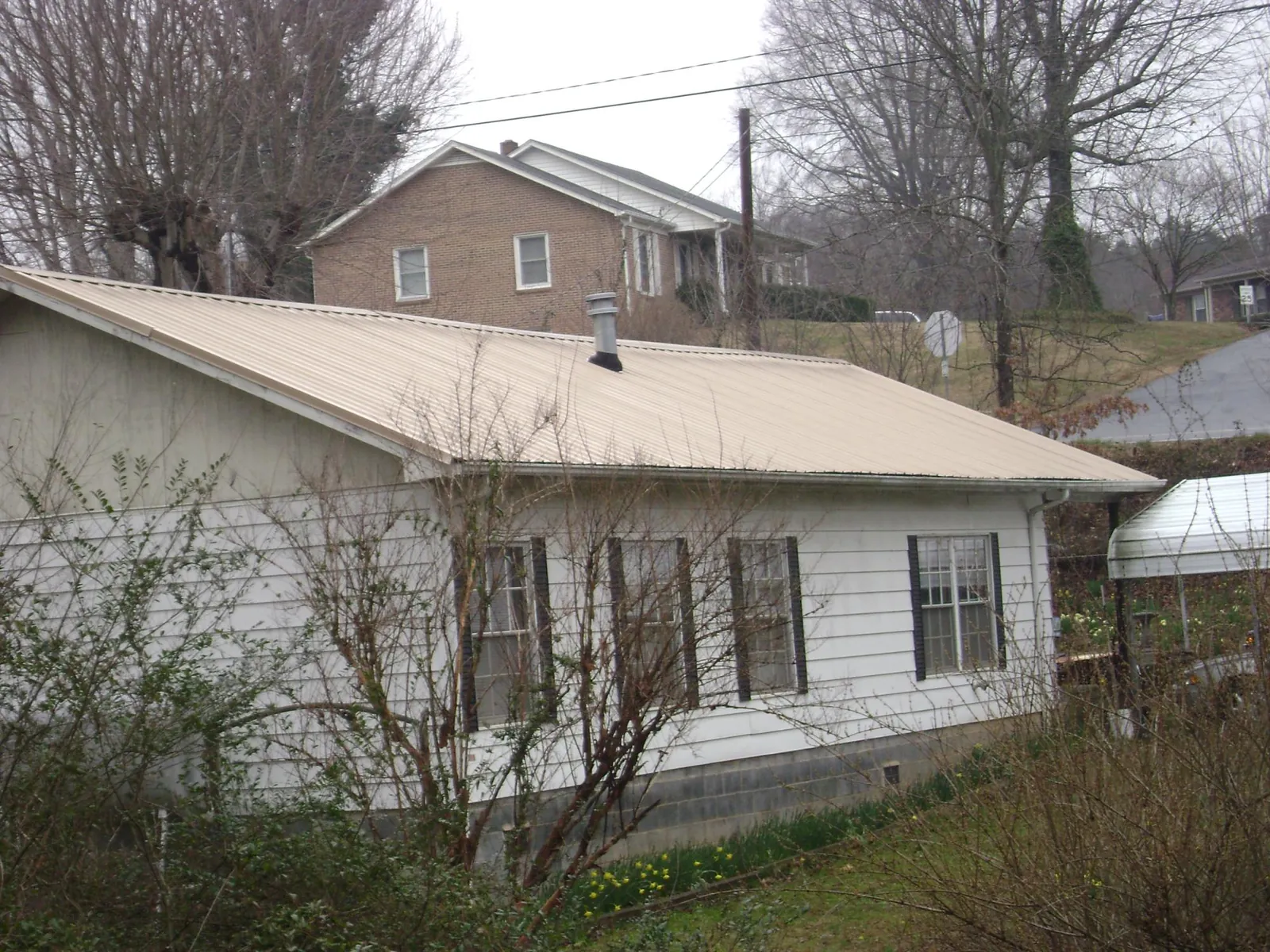 Tan metal roof on a white sided house set into a hillside — Commercial Roofing by Roofing Brothers in Royal Oak